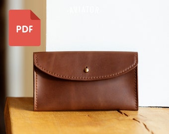 Puede incluir: Una cartera de cuero marrón con cierre de solapa y un botón de latón. La cartera está sobre una superficie de madera.