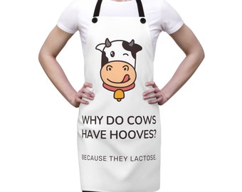 May include: White apron with a cartoon cow graphic and the text "WHY DO COWS HAVE HOOVES? BECAUSE THEY LACTOSE." The cow has a black and white head, a pink tongue, and a gold bell.