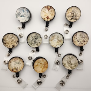 May include: Ten vintage map themed retractable badge holders with black frames and clear plastic straps. The maps feature different designs, including a compass, a ship, and a world map.