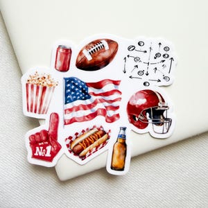 May include: A sticker sheet featuring watercolor illustrations of American football themes, including a brown football, a red helmet, a waving American flag, a hot dog, a red foam finger with the text No1, popcorn, a soda can, a beer bottle, and a play diagram.