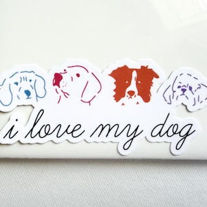 May include: A white sticker featuring four stylized dog head illustrations in blue, red, orange, and purple outlines. Below the dogs, the black cursive text reads i love my dog. The sticker has a die-cut shape that follows the contours of the dogs.