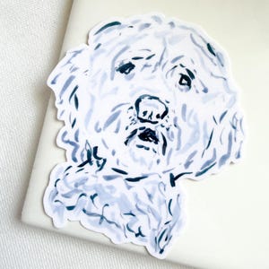 May include: A die-cut sticker featuring a stylized illustration of a dog with curly fur. The artwork uses shades of light blue and dark navy ink strokes to define the facial features, nose, and textured coat of the canine against a white background.