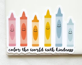 May include: A sticker featuring six colorful crayons in pink, orange, yellow, and blue shades, each with a simple black smiley face. Below the crayons, the text reads "color the world with kindness" in a black, cursive, handwritten-style font.