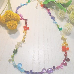 May include: A multi-colored gemstone necklace featuring a variety of faceted and smooth beads in shades of red, orange, yellow, green, blue, and purple. The necklace includes a gold-toned metal chain with a lobster clasp closure at the top.