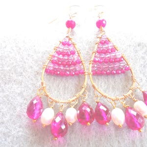 May include: Gold-coloured chandelier earrings with pink and white beads. The earrings have a teardrop shape with a pyramid of small pink beads at the top. Dangling from the bottom are larger pink and white teardrop-shaped beads.