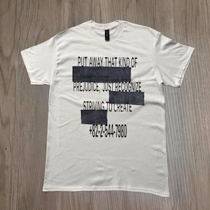 Puede incluir: Camiseta blanca con texto negro y rectángulos gris oscuro. El texto dice: "PUT AWAY THAT KIND OF PREJUDICE, JUST RECOGNIZE STRIVING TO CREATE +82-2-544-7980". La camiseta está hecha de un material suave.