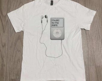 Könnte beinhalten: Ein weißes kurzärmeliges T-Shirt mit einer Grafik eines grauen digitalen Musikplayers und weißen kabelgebundenen Ohrhörern. Auf dem Bildschirm des Musikplayers steht der Text "music to my ears." Das T-Shirt hat einen Rundhalsausschnitt.