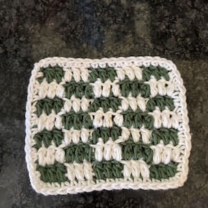 Puede incluir: Un posavasos cuadrado tejido a crochet con un patrón de cuadros blancos y verdes.