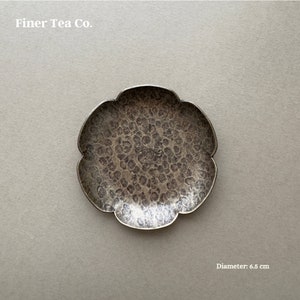 May include: A small, hammered metal dish with a scalloped edge. The dish is silver-toned and has a diameter of 2.5 inches. The text "Finer Tea Co." is at the top. The diameter is 2.5 inches.