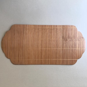 May include: A long, rectangular, natural-colored bamboo serving tray with a slightly curved edge and a woven pattern. The tray has a gold-colored finish.