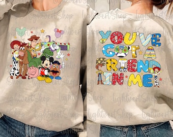 Może przedstawiać: Beżowa bluza z grafiką postaci z Toy Story z przodu i napisem "You've Got a Friend in Me" z tyłu.