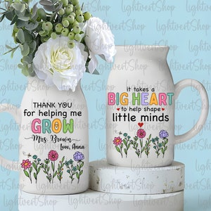 May include: Two white ceramic mugs with colorful floral designs and text. The mug on the left says "Thank you for helping me grow. Mrs. Brown Love, Anna". The mug on the right says "It takes a big heart to help shape little minds".