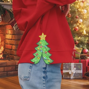 May include: A red sweatshirt with a green glitter Christmas tree appliqué on the back. The tree has a gold star on top and colorful lights.