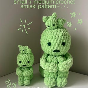 Puede incluir: Dos figuras de ganchillo verdes, una pequeña y otra mediana, con un diseño único. Las figuras tienen un cuerpo redondo, brazos pequeños y una cabeza con una figura más pequeña encima. El texto "small + medium crochet smiski pattern" está en la parte superior.