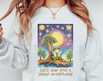 Può includere: Una felpa grigia con una grafica di una rana verde seduta su un ramo di albero che legge un libro sotto una luna piena e stelle. Il testo "Let's leap into a great adventure!" è stampato sotto la grafica.