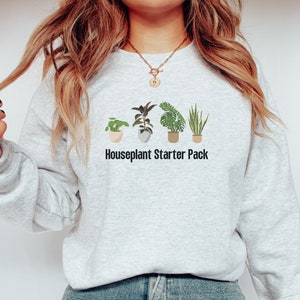 Puede incluir: Una sudadera gris con un gráfico de cinco plantas en maceta y el texto "Houseplant Starter Pack".