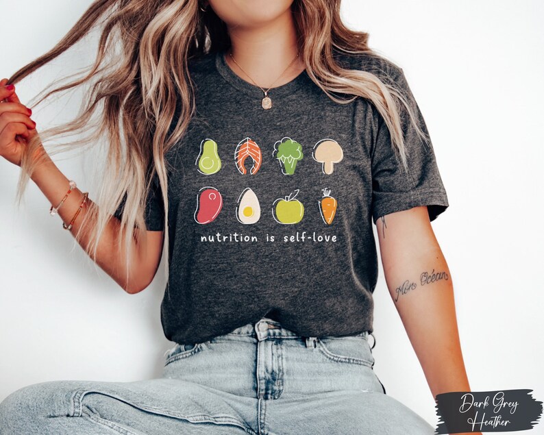 Puede incluir: Camiseta de color gris oscuro jaspeado con un gr&aacute;fico de varios alimentos saludables y el texto "nutrition is self-love".