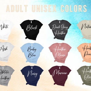 Pu&ograve; includere: Una selezione di t-shirt unisex in vari colori, tra cui bianco, nero, grigio scuro melange, naturale, cenere, azzurro, malva melange, pesca melange, grigio melange atletico, blu navy, bordeaux e oliva melange. Le t-shirt sono esposte su uno sfondo marrone chiaro.