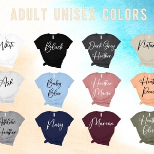 Puede incluir: Una selecci&oacute;n de camisetas unisex en varios colores, incluyendo blanco, negro, gris oscuro jaspeado, natural, ceniza, azul beb&eacute;, malva jaspeado, melocot&oacute;n jaspeado, gris jaspeado atl&eacute;tico, azul marino, granate y oliva jaspeado. Las camisetas se muestran sobre un fondo marr&oacute;n claro.