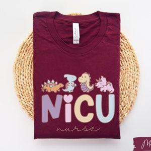 Puede incluir: Camiseta de color granate con un gr&aacute;fico de dinosaurios y el texto "NICU nurse".