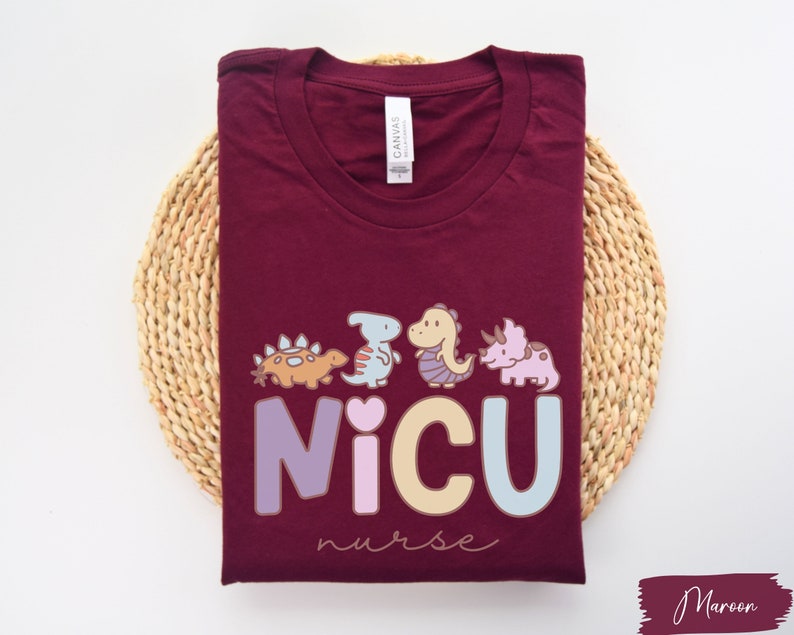 Puede incluir: Camiseta de color granate con un gr&aacute;fico de dinosaurios y el texto "NICU nurse".