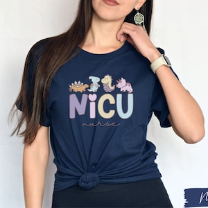 Puede incluir: Una camiseta azul marino con un gr&aacute;fico de dinosaurios y el texto "NICU nurse".