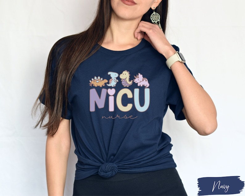 Puede incluir: Una camiseta azul marino con un gr&aacute;fico de dinosaurios y el texto "NICU nurse".