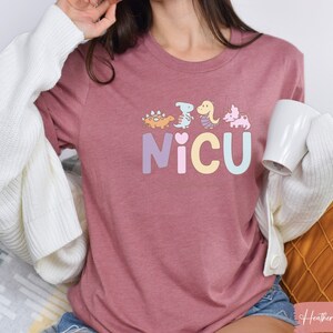 Puede incluir: Una camiseta de color malva jaspeado con un gr&aacute;fico de dinosaurios de color pastel y la palabra "NICU" en colores pastel.