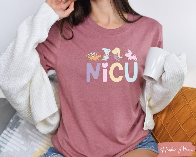 Puede incluir: Una camiseta de color malva jaspeado con un gr&aacute;fico de dinosaurios de color pastel y la palabra "NICU" en colores pastel.