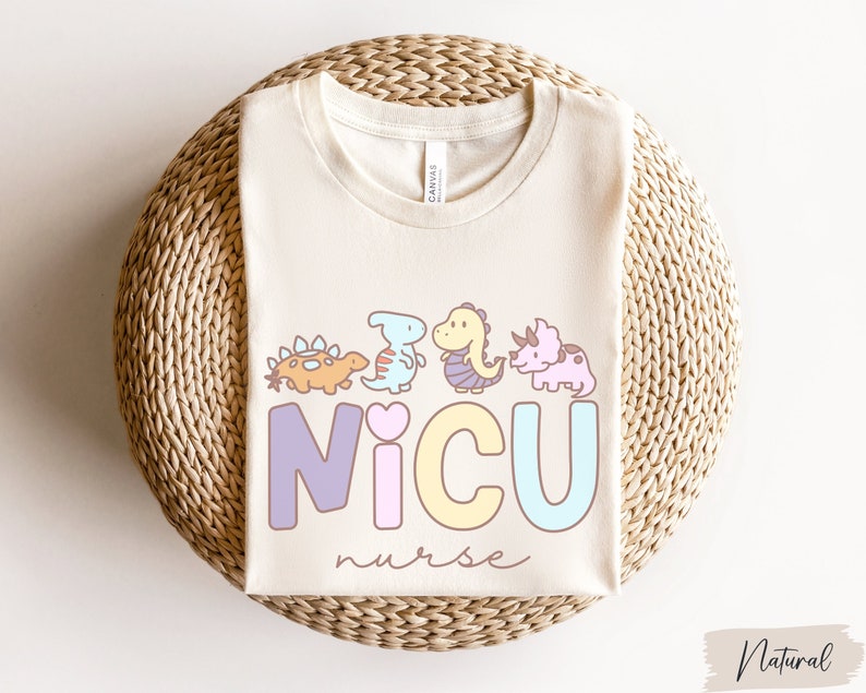 Puede incluir: Una camiseta de color natural con un gr&aacute;fico de dinosaurios y el texto "NICU nurse".