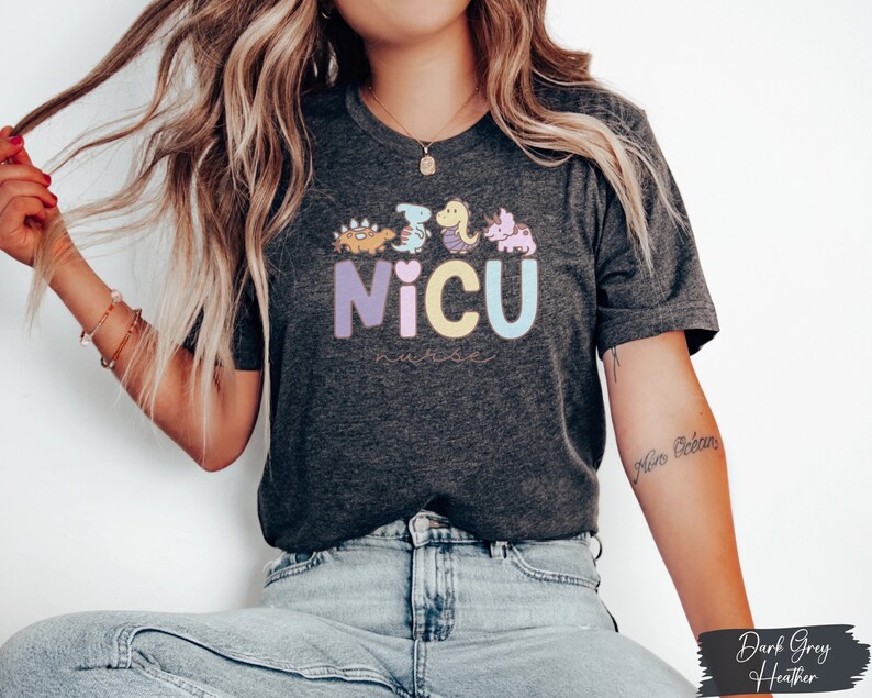Puede incluir: Una camiseta de color gris oscuro jaspeado con un gr&aacute;fico de dinosaurios coloridos y el texto "NICU Nurse".