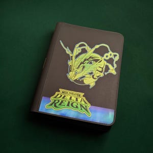 May include: A dark brown binder featuring a large, stylized green and yellow graphic of a dragon-like creature. Below the creature, a vibrant label displays the text "MEGA EVOLUTION DELTA REIGN" in bold yellow and green lettering.