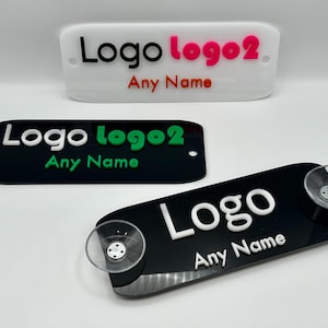 Peut inclure: Trois enseignes de logo personnalisées. L'une est blanche avec du texte rose et rouge, une autre est noire avec du texte vert et blanc, et la troisième est noire avec du texte blanc et des ventouses. Le texte indique "Logo logo2 Any Name".