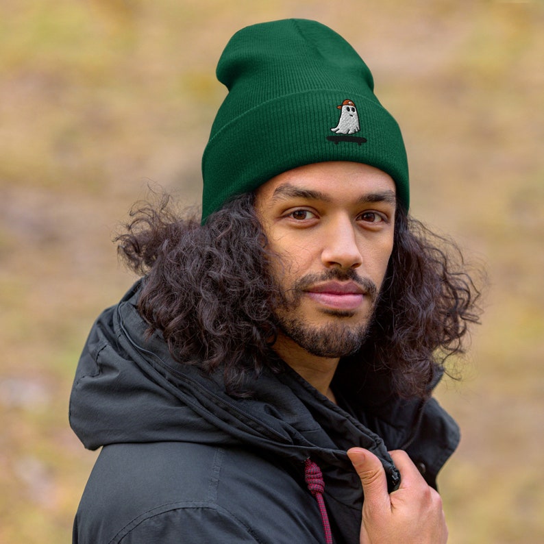 May include: A dark green beanie with a white ghost wearing a red hat and skateboarding embroidered on the front.