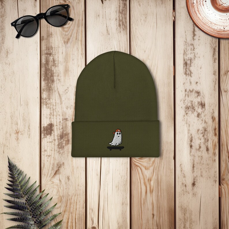 May include: A green beanie with a white ghost wearing a red hat and skateboarding embroidered on the front.