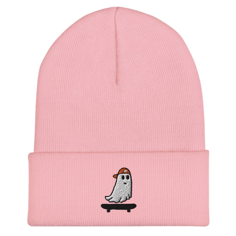 May include: Pink beanie with an embroidered design of a ghost wearing a baseball cap and skateboarding.