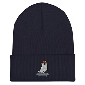 May include: A navy blue beanie with a white embroidered ghost wearing an orange hat and riding a skateboard.