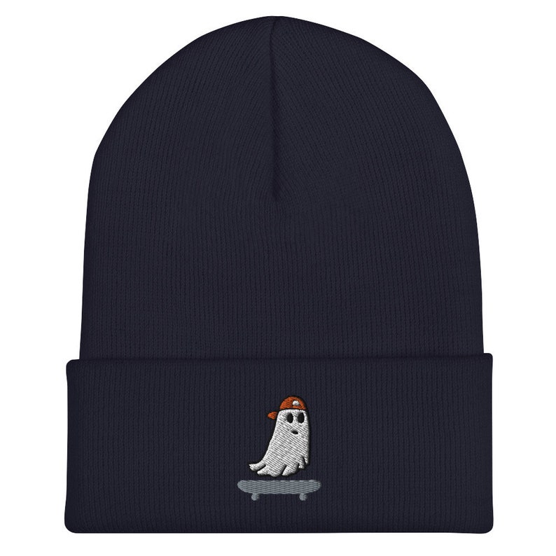 May include: A navy blue beanie with a white embroidered ghost wearing an orange hat and riding a skateboard.
