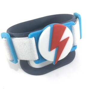 May include: A blue, white, and red lightning bolt wristband. The wristband has a white strap, blue accents, and a circular emblem with a red lightning bolt on a white background. The band is approximately 5 cm wide.