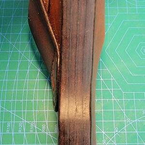 以下が含まれることがあります： フラップ付きの茶色の革製ホルスター。ホルスターは緑色のカッティングマットの上にあります。