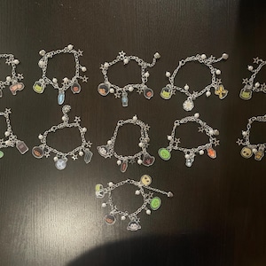 May include: A collection of silver charm bracelets with various Halloween-themed charms. Each bracelet features a chain with star-shaped accents and small white beads. The charms include pumpkins, ghosts, and other spooky designs.