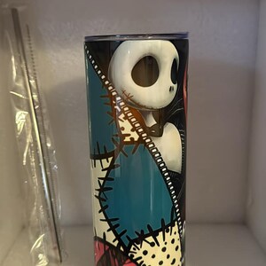 May include: A stainless steel tumbler with a colorful patchwork design featuring a black and white illustration of Jack Skellington from The Nightmare Before Christmas.