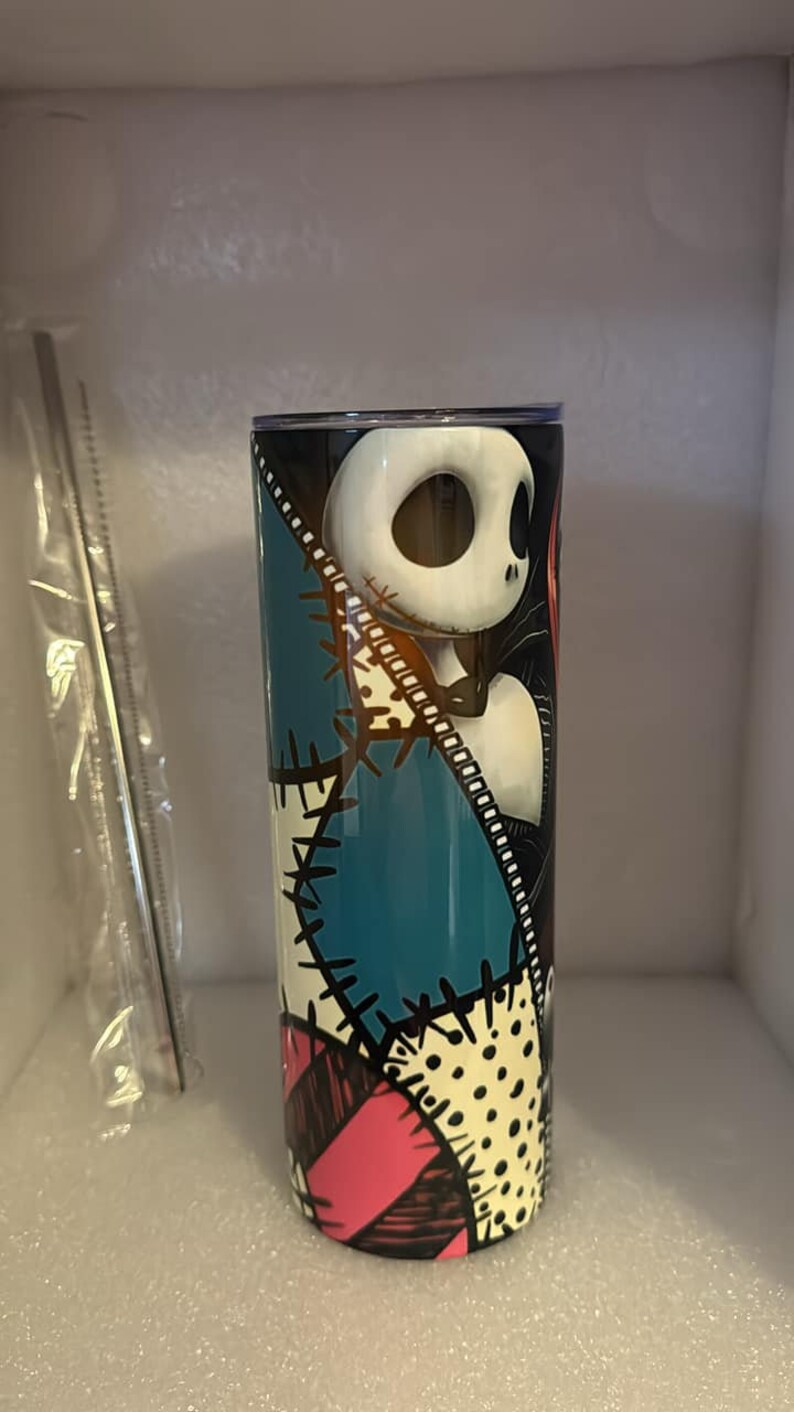 May include: A stainless steel tumbler with a colorful patchwork design featuring a black and white illustration of Jack Skellington from The Nightmare Before Christmas.