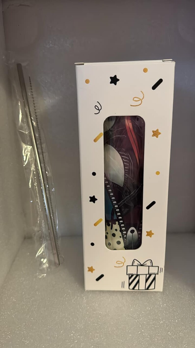 May include: A white box with a colorful design featuring a black and white gift box, stars, and confetti. The box contains a reusable straw with a colorful design.