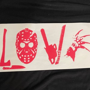 Puede incluir: Una pegatina de vinilo blanco con la palabra "LOVE" escrita en rosa. Las letras están formadas por iconos de películas de terror, incluyendo una máscara de hockey, una motosierra, un machete y un guante de Freddy Krueger.