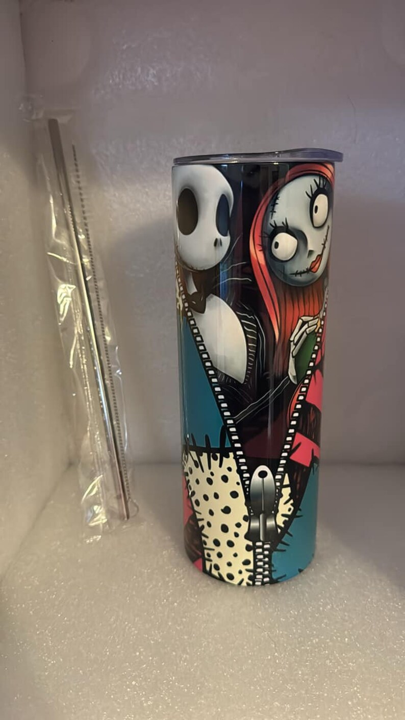 May include: A stainless steel tumbler with a colorful design featuring Jack Skellington and Sally from The Nightmare Before Christmas. The design includes a zipper and polka dots.
