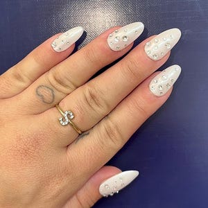 Può includere: Unghie bianche ovali con un design di piccoli strass trasparenti.