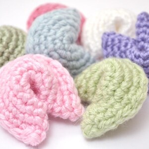 May include: A collection of crocheted fortune cookie charms in various colors, including light green, pink, light blue, purple, and white.