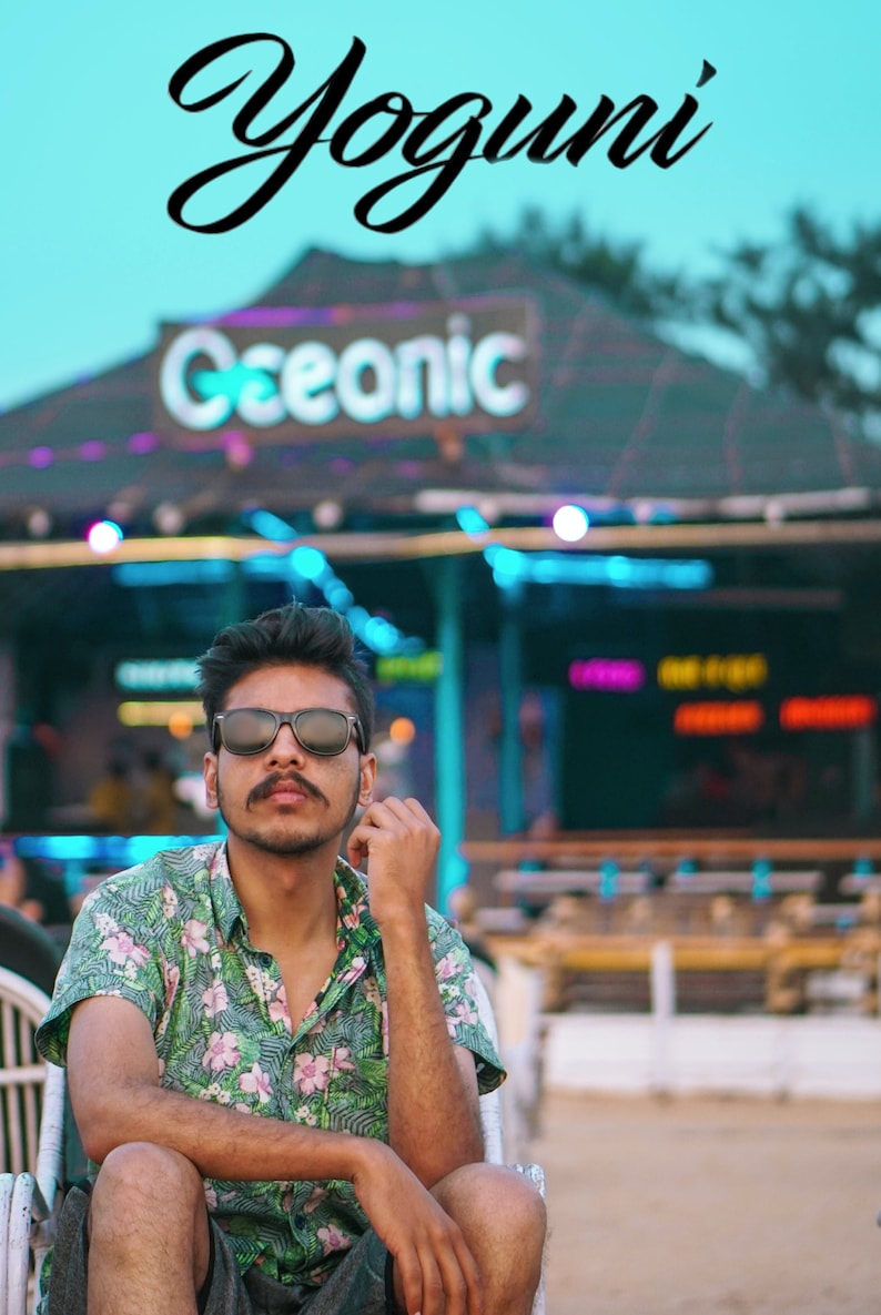 May include: A person wearing sunglasses and a floral shirt sits in a chair. The word "Yoguni" is written in cursive at the top of the image. The sign behind the person says "Ceeonic". The background is a beach setting.