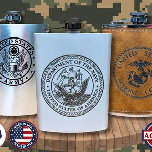 May include: Three stainless steel flasks with military emblems. One is silver with a US Army seal, another is white with a US Navy seal, and the third is brown with a US Marine Corps seal. The flasks are displayed on a wooden surface.